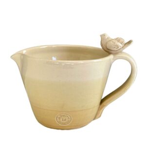 A cream and yellow ceramic pitcher with a bird on the handle Description automatically generated