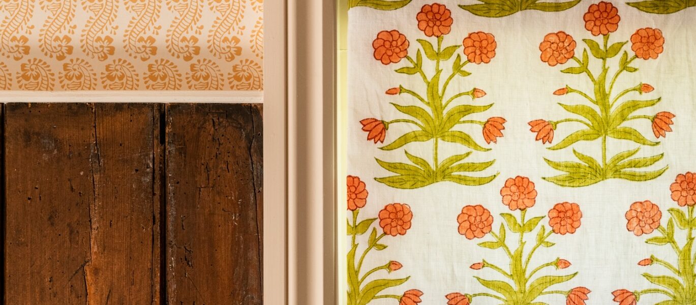 A window with a white frame and a white curtain with orange flowers on it Description automatically generated
