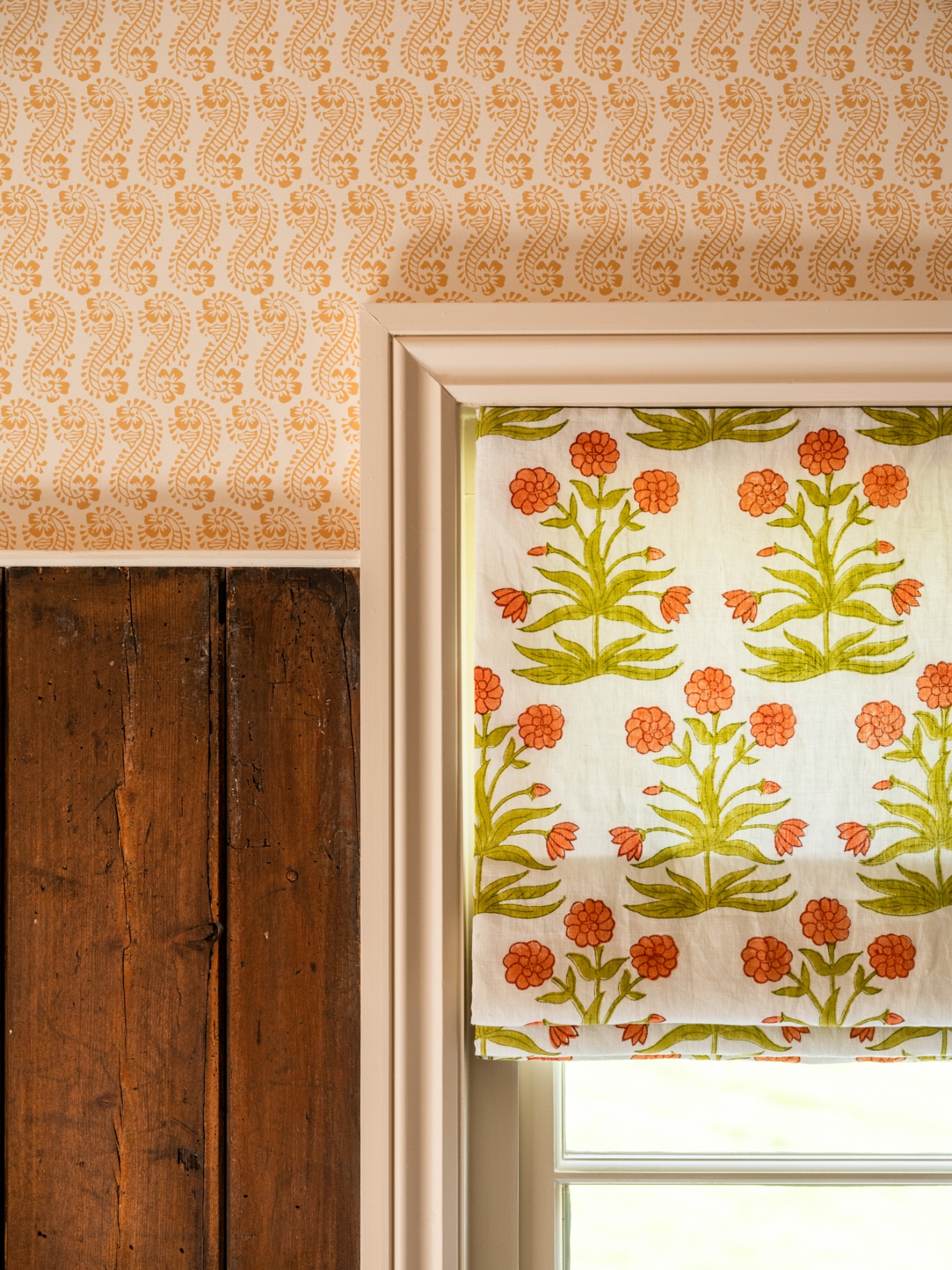A window with a white frame and a white curtain with orange flowers on it Description automatically generated