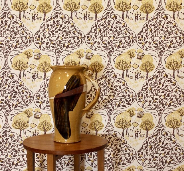 A wallpaper behind a vase which depicts a charming countryside scene and is available in seven colourways.
