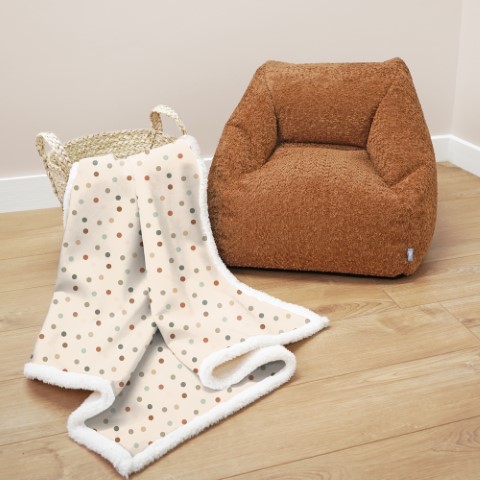 a comfy lookig blanket with a dotty design next to a brown beanbag seat