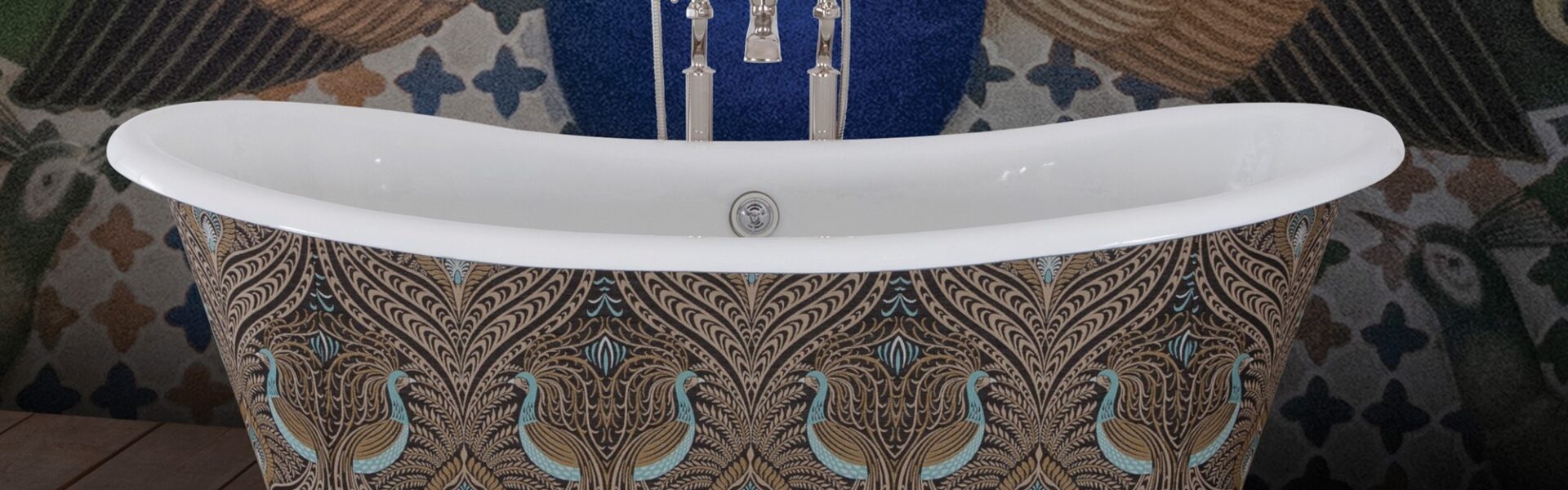 The image showcases a luxurious freestanding bathtub with a bold maximalist design, set against a similarly ornate background. The exterior of the tub is adorned with a peacock feather pattern, rendered in a palette of rich browns, golds, and teals. This intricate pattern gives the tub an opulent and bespoke appearance. The bathtub fixtures are traditional in style with a chrome finish, adding a touch of timeless elegance to the modern expression of maximalism. Behind the bathtub, a peacock-themed wall mural complements the tub's design, featuring an expanded tail in a display of vibrant green, blue, and gold hues, set against a deep blue background. The floor is a wooden texture, providing a warm, natural contrast to the cool tones of the tub and wall. The overall effect is one of lavishness and artistic flair, making a striking statement in this maximalist bathroom setting.