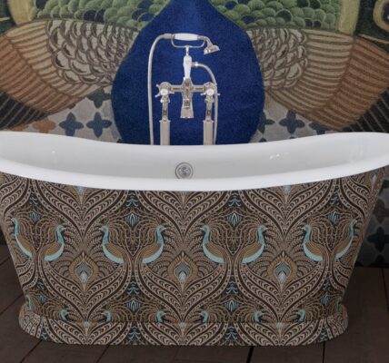 The image showcases a luxurious freestanding bathtub with a bold maximalist design, set against a similarly ornate background. The exterior of the tub is adorned with a peacock feather pattern, rendered in a palette of rich browns, golds, and teals. This intricate pattern gives the tub an opulent and bespoke appearance. The bathtub fixtures are traditional in style with a chrome finish, adding a touch of timeless elegance to the modern expression of maximalism. Behind the bathtub, a peacock-themed wall mural complements the tub's design, featuring an expanded tail in a display of vibrant green, blue, and gold hues, set against a deep blue background. The floor is a wooden texture, providing a warm, natural contrast to the cool tones of the tub and wall. The overall effect is one of lavishness and artistic flair, making a striking statement in this maximalist bathroom setting.