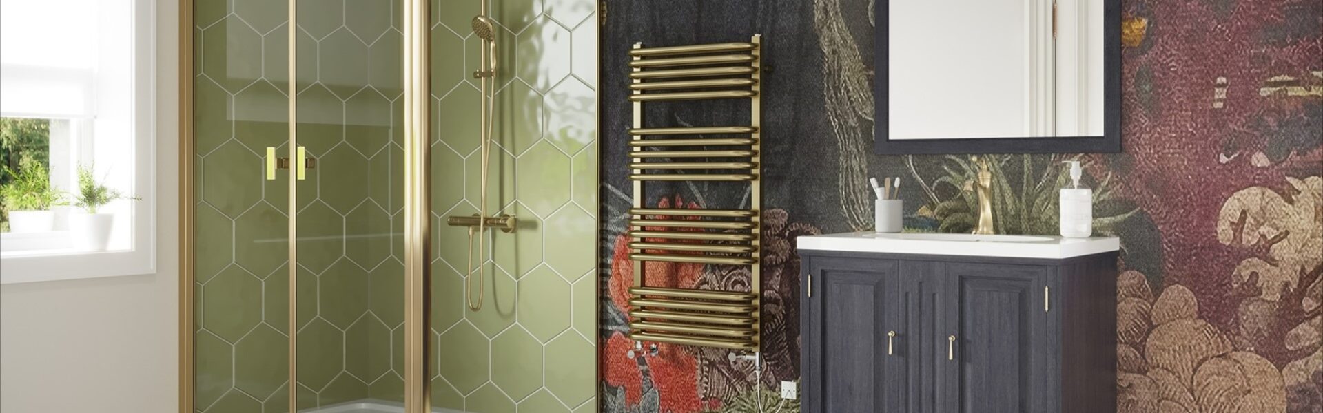The image features a stylish bathroom with a contemporary design that incorporates brass elements. The focal point is a brushed brass dual fuel towel rail, which stands out against a dark, intricately patterned wallpaper that depicts a lush forest scene with hints of wildlife and florals in deep reds and greens. The shower enclosure showcases a geometric brass frame with clear glass, complementing the towel rail and adding a touch of modern luxury. The vanity unit is a classic dark wood with brass handles, contrasting the white basin above it and the white and black diamond patterned tile floor below. The space is well-lit, and there is a white-framed mirror above the vanity that reflects the natural light coming from the window. The overall aesthetic is one of elegance and warmth, with the brass accents lending a timeless yet trendy feel to the bathroom, exemplifying how brass fixtures can add sophistication to a home.