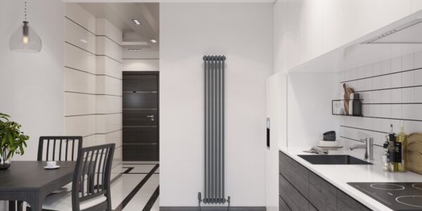 a modern kitchen and dining area with a minimalist design. The space is dominated by a monochromatic color scheme, featuring shades of white, black, and gray. A sleek, dark dining table with four matching chairs is placed on the left side of the image, under a simple hanging pendant light. To the right, the kitchen area is equipped with white cabinetry and black countertops. The backsplash consists of white rectangular tiles with dark grouting, and there are various kitchen items like pots, a cutting board, and bottles of oil on the counter. In the center of the image is a tall, vertical, anthracite-colored column radiator, and there's a modern dark door in the background on the left. The flooring is a geometric pattern of white and black tiles that complement the overall contemporary aesthetic of the room.