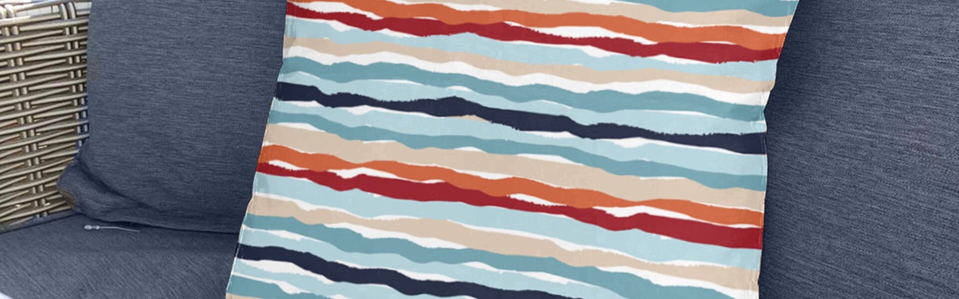 A square, coral and white striped throw pillow sits on a couch with a blue and white striped pattern.