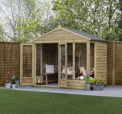 A brown wooden summerhouse is located in a garden. The shed has two doors and four windows. A wooden fence runs along the edge of the garden.