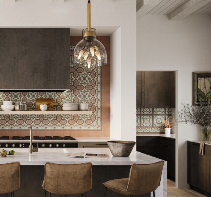 A kitchen with a stainless-steel stovetop oven and a black pendant light hanging from the ceiling. The countertop is a light-coloured stone with a mottled pattern. There are grey veined tiles on the wall behind the stovetop.