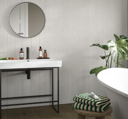 A small bathroom featuring modern reeded wooden wall-panelling with a white sink, mirror, and bathtub.