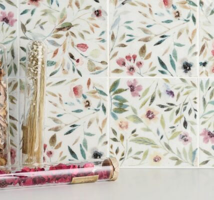 A close-up of a square white tile with a floral pattern in shades of blue and green.