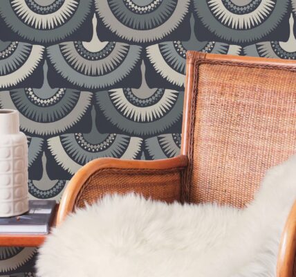 The wallpaper has a blue background with a white and grey feather pattern. The feathers are arranged in a staggered pattern, and they look like they are blowing in the wind. There is a brown armchair in the foreground, and a white vase and book on a side table in the background.