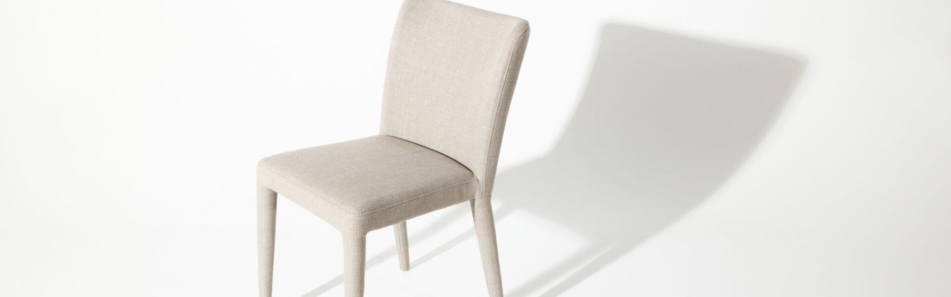 A modern white chair with a simple design casts a shadow on a white background