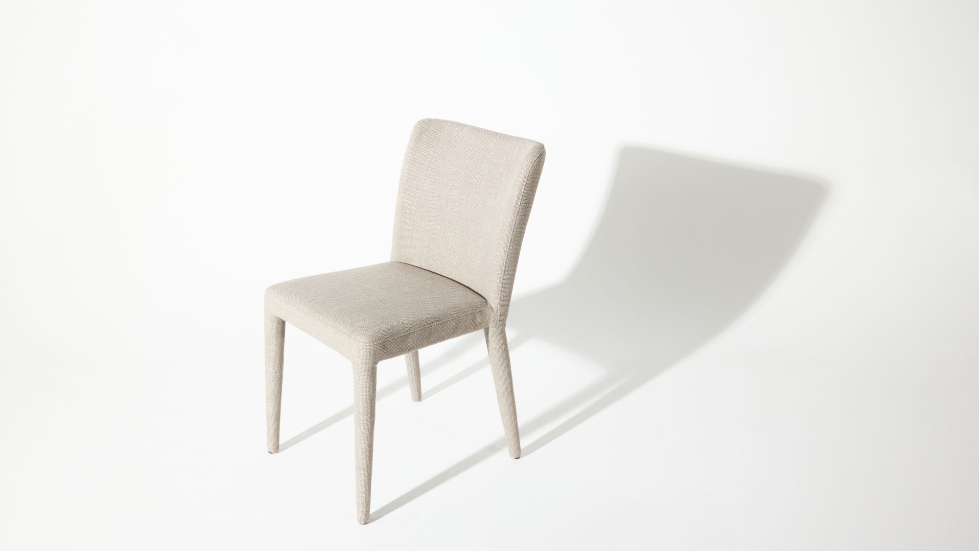 A modern white chair with a simple design casts a shadow on a white background