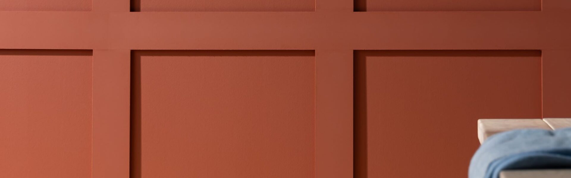 A red wooden panelled wall with a simple, light coloured wooden table in front of it.