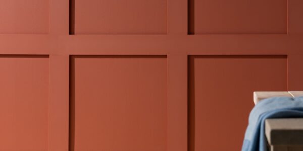 A red wooden panelled wall with a simple, light coloured wooden table in front of it.