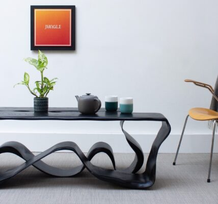 A coffee table with distinctive feet and chair in a living room with an orange image on the wall.