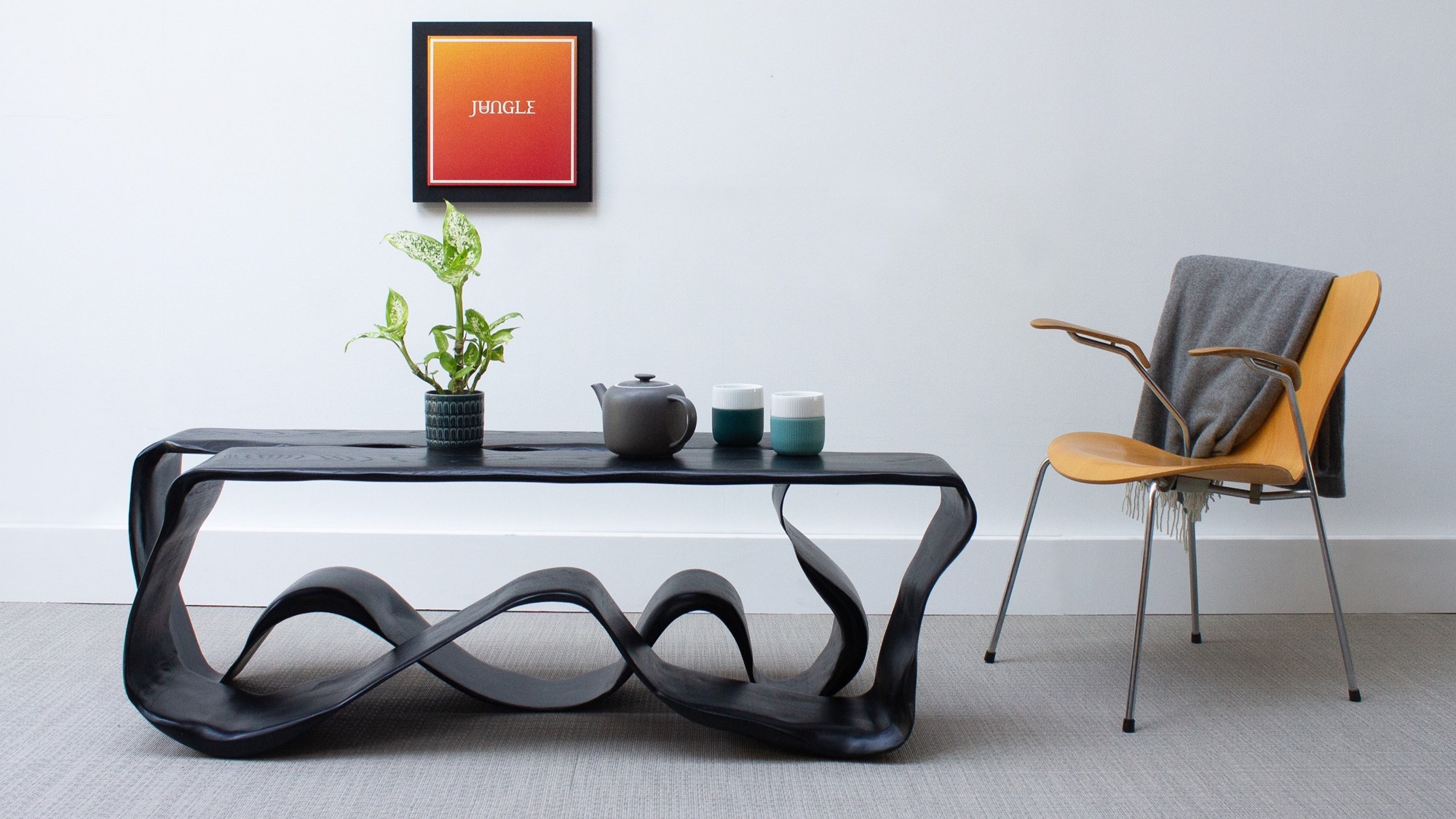 A coffee table with distinctive feet and chair in a living room with an orange image on the wall.