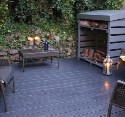 A relaxing outdoor space featuring a dark wicker furniture set and a fire pit. The wicker furniture includes two chairs, a loveseat, and a small table. The fire pit is made of black metal.