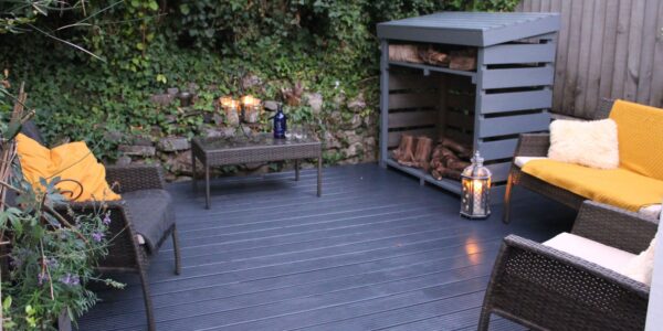 A relaxing outdoor space featuring a dark wicker furniture set and a fire pit. The wicker furniture includes two chairs, a loveseat, and a small table. The fire pit is made of black metal.
