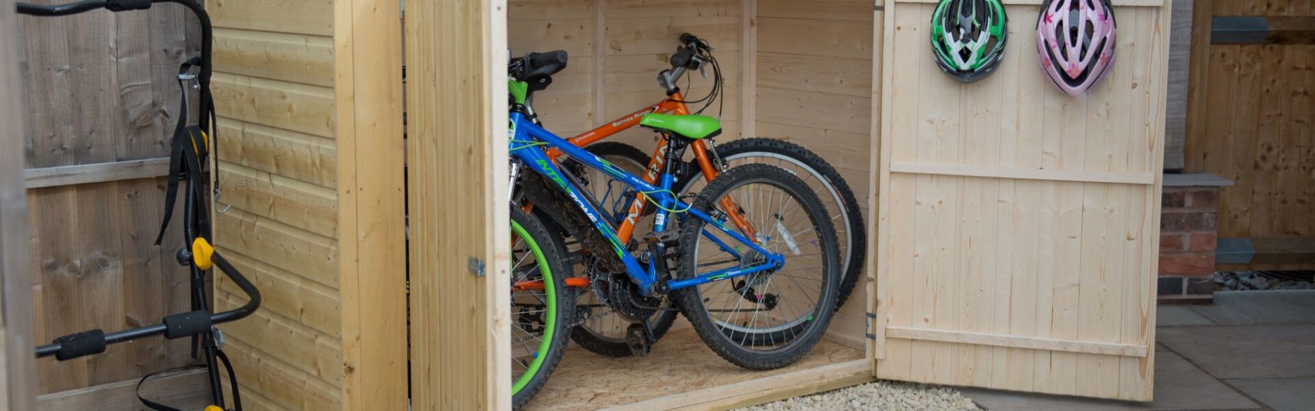 Wooden bike shed with double doors open, revealing two bicycles inside.