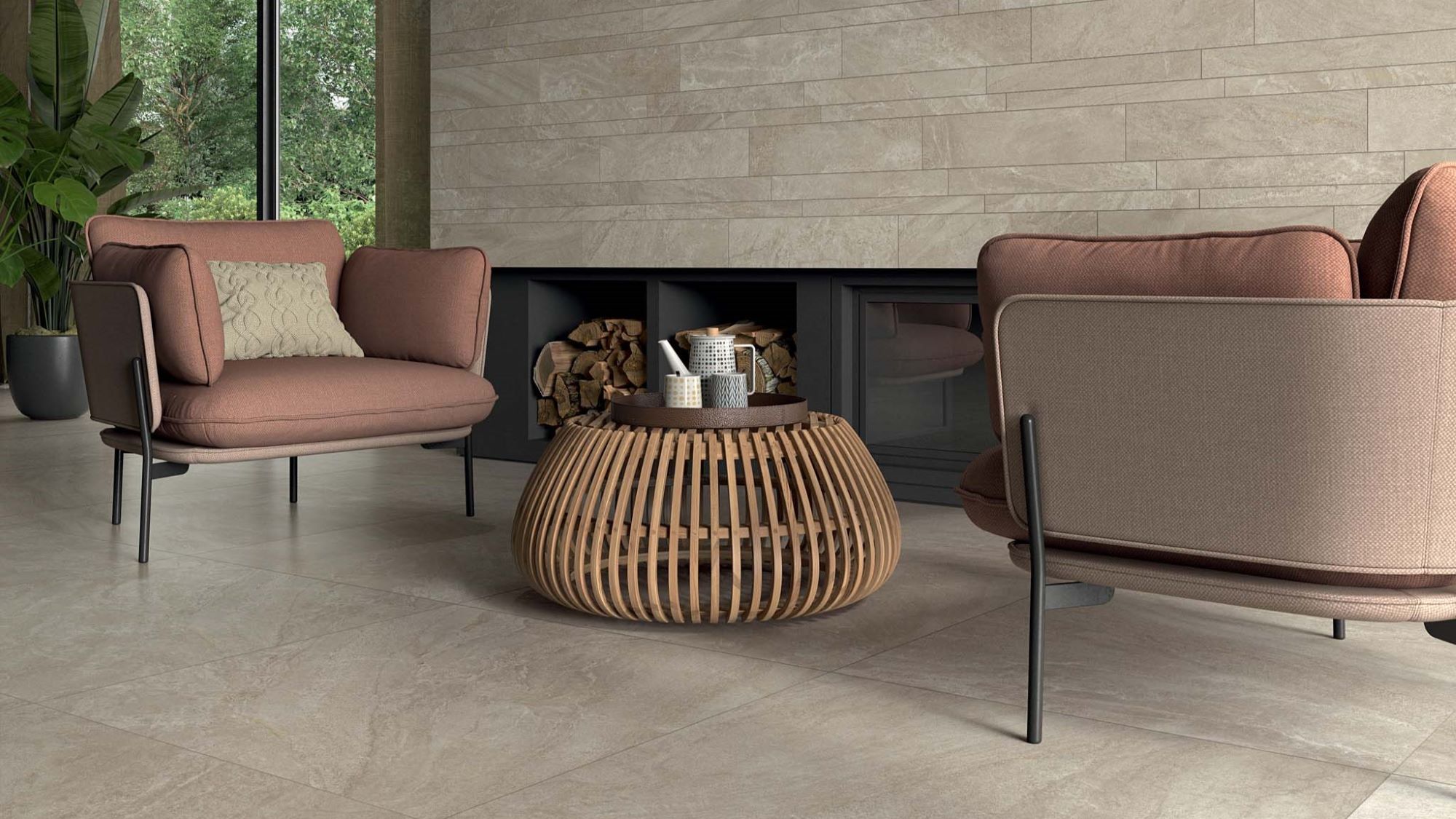 The image shows a spacious and modern living room with two comfortable armchairs facing each other. The chairs have a reddish-brown fabric covering and a black metal frame. A round coffee table with a woven design sits between them. The floor is covered with large, light-coloured tiles, and the walls are adorned with light grey tiles arranged in a brick pattern.