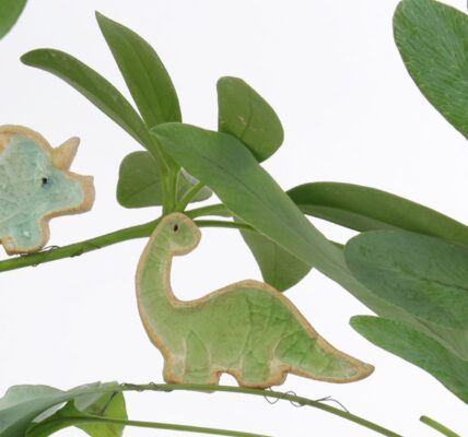 Two ceramic dinosaur figurines perched on a plant. One is a blue triceratops and the other is a green brontosaurus.
