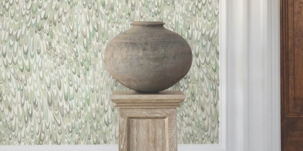 A large, earthy-toned clay pot sits on a wooden pedestal against a backdrop of a light green wallpaper with swirling, abstract feather-like patterns.