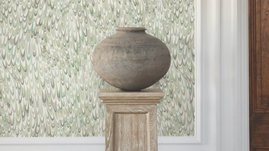 A large, earthy-toned clay pot sits on a wooden pedestal against a backdrop of a light green wallpaper with swirling, abstract feather-like patterns.