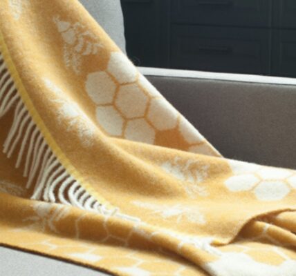 The throw features a distinctive pattern of bees and honeycombs, woven into a soft, mustard yellow wool. The fringes add a touch of texture and style. It seems to be a cozy and visually appealing piece that would complement a variety of home decor styles.