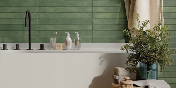 The image shows a modern bathroom with a white bathtub, a green tiled wall, and a variety of accessories, including a plant, towels, and a soap dispenser. The overall aesthetic is clean, minimalist, and inviting.