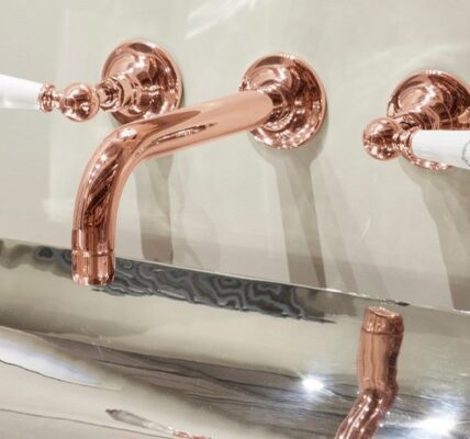 A luxurious bathroom vanity with a copper-coloured tap set. The tap has a classic design with white porcelain handles. The basin is rectangular and made of polished stainless steel. The overall aesthetic of the bathroom is elegant and sophisticated.