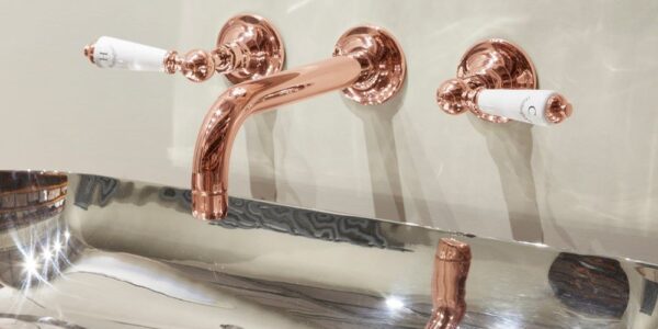 A luxurious bathroom vanity with a copper-coloured tap set. The tap has a classic design with white porcelain handles. The basin is rectangular and made of polished stainless steel. The overall aesthetic of the bathroom is elegant and sophisticated.