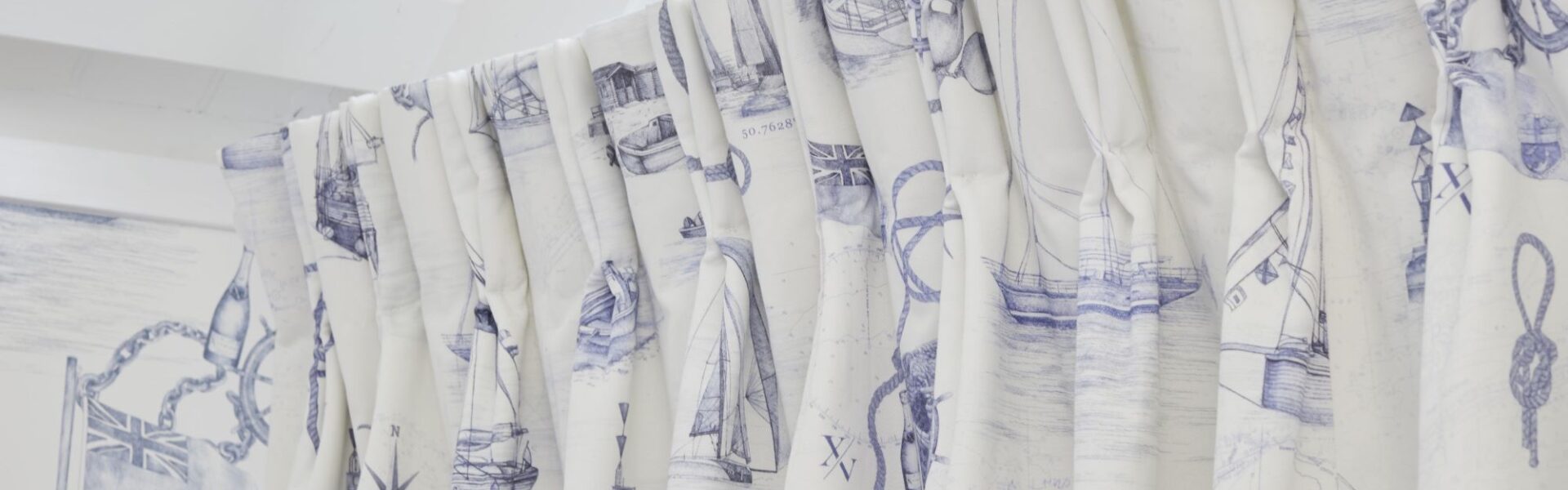 The curtains are white with a blue nautical pattern featuring boats, ships, and anchors. The rod is white and appears to be curved.