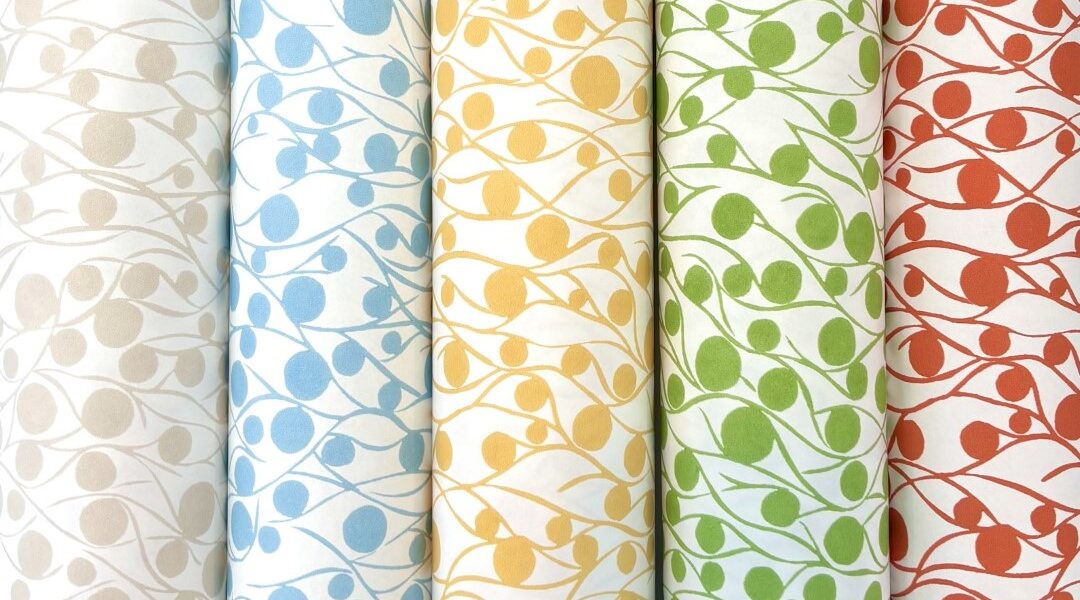 Five rolls of fabric with a repeating pattern of circles and lines. The circles are different colours on each roll: cloud, blue, yellow, green, and coral. The lines are white on each roll and create a wavy pattern that connects the circles.