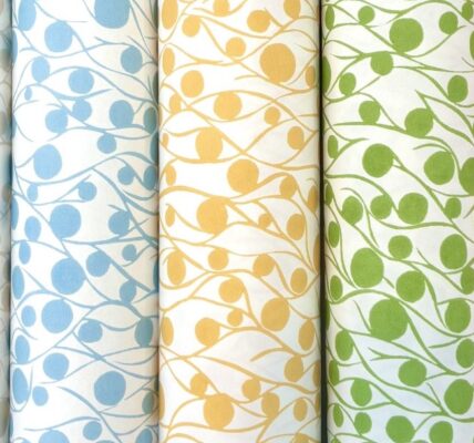 Five rolls of fabric with a repeating pattern of circles and lines. The circles are different colours on each roll: cloud, blue, yellow, green, and coral. The lines are white on each roll and create a wavy pattern that connects the circles.
