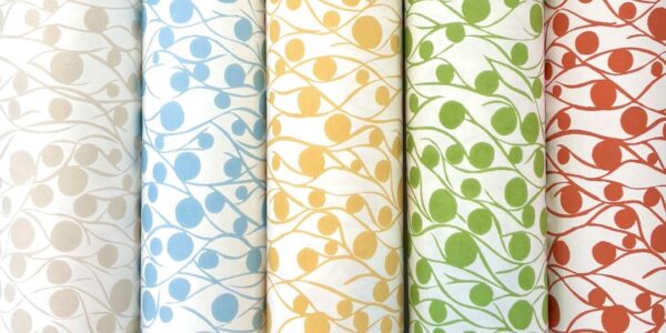 Five rolls of fabric with a repeating pattern of circles and lines. The circles are different colours on each roll: cloud, blue, yellow, green, and coral. The lines are white on each roll and create a wavy pattern that connects the circles.