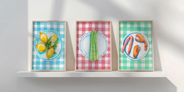 Three framed illustrations of food on plates. The left image shows lemons on a blue and white plate against a blue and white gingham background. The middle image shows asparagus on a blue and white plate against a red and white gingham background. The right image shows lobster claws on a blue and white plate against a green and white gingham background.