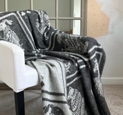 A cosy grey throw blanket with a playing card pattern draped over a white armchair.