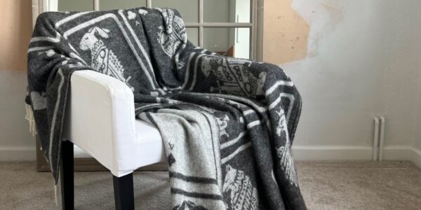 A cosy grey throw blanket with a playing card pattern draped over a white armchair.