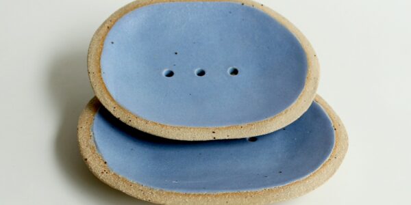 Two blue ceramic soap dishes with a raised rim and drainage holes. The soap dishes are slightly textured and have a natural, organic look.