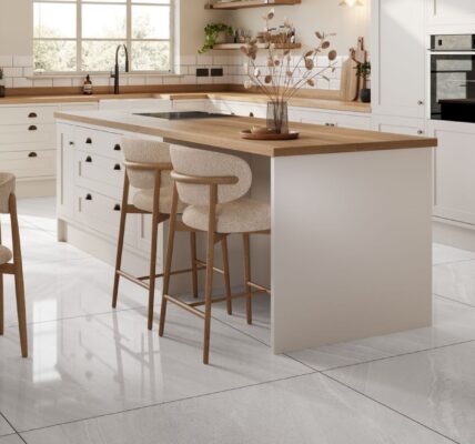 A spacious and stylish kitchen with a large island and a dining area. The kitchen has a modern design with white cabinets, a wooden countertop, and a white tile floor.