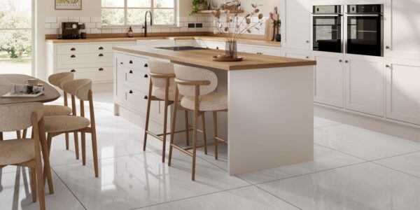 A spacious and stylish kitchen with a large island and a dining area. The kitchen has a modern design with white cabinets, a wooden countertop, and a white tile floor.