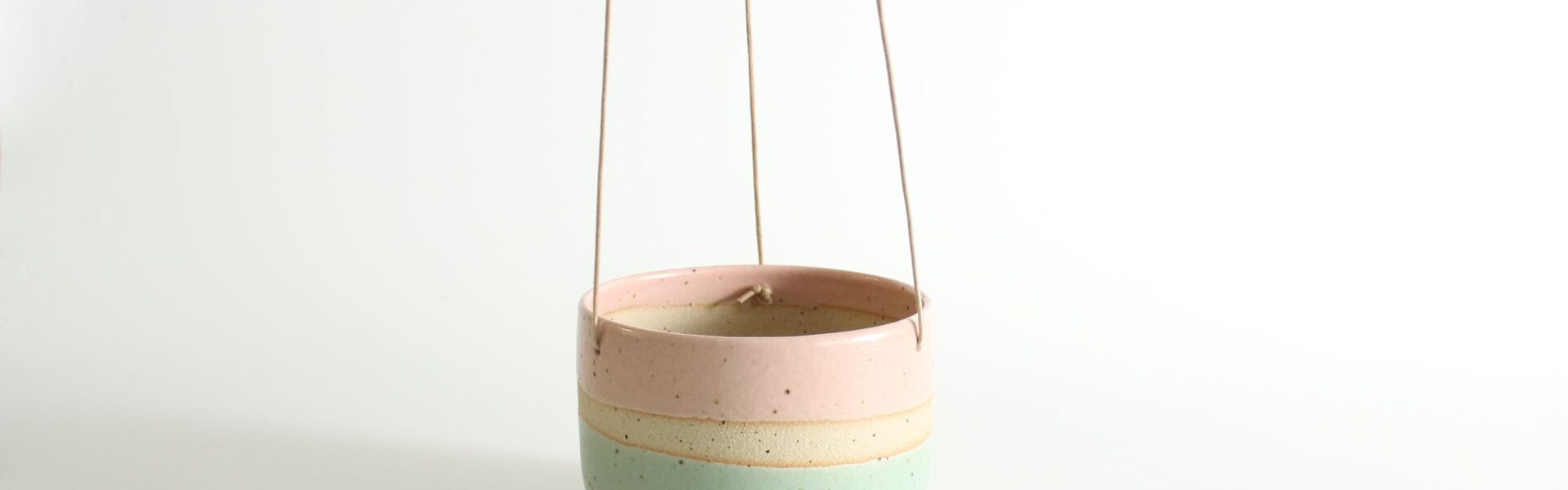 A hanging planter with a pastel pink, cream, and mint green colour block design
