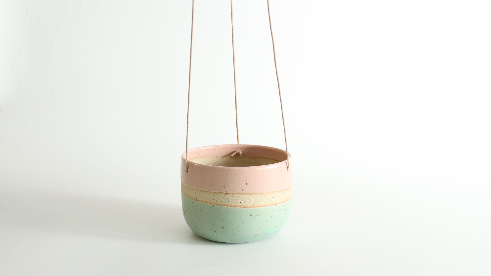 A hanging planter with a pastel pink, cream, and mint green colour block design