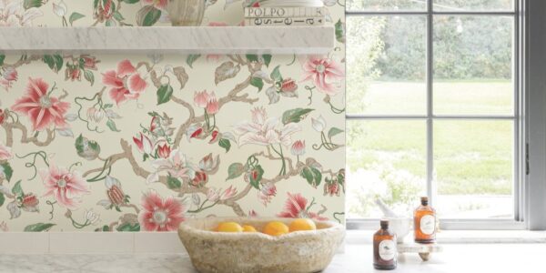 A bright kitchen featuring Ronald Redding Classics Marguerite Vine wallpaper in a pink and green botanical pattern, white marble countertops, a vintage stone bowl filled with oranges, and two bottles on the counter.