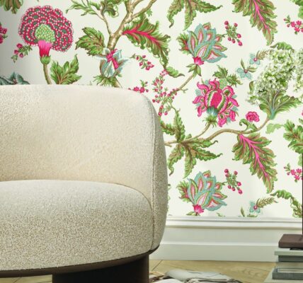 A close-up shot of a cream-coloured, rounded boucle fabric chair with a dark wood base, positioned in front of a wall with a vibrant floral wallpaper featuring pink, green, and white flowers and leaves.