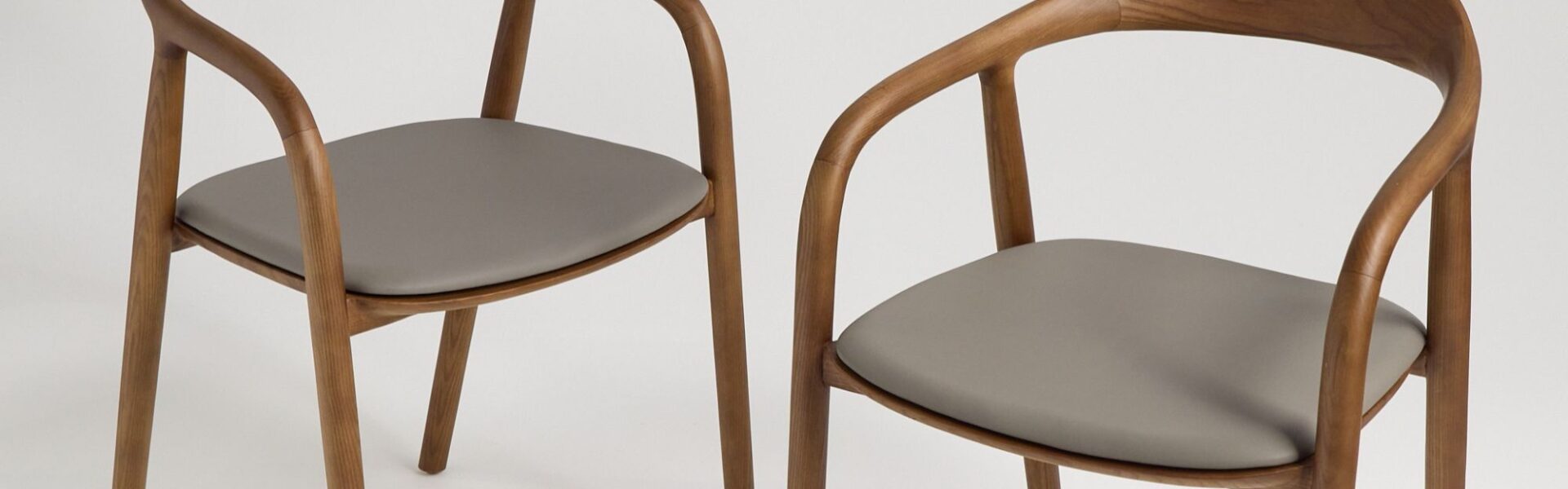 A pair of contemporary wooden dining chairs with curved backs and grey upholstered seats.