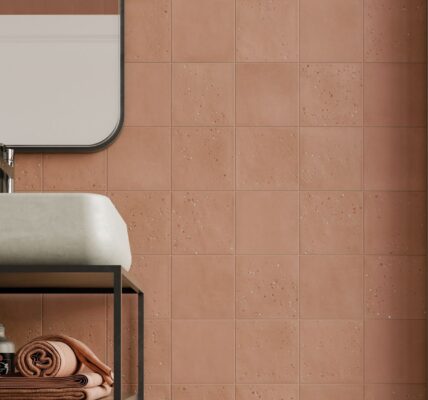 A bathroom wall tiled with square, textured terracotta tiles in a grid pattern. A white sink and black framed mirror are partially visible.