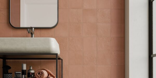A bathroom wall tiled with square, textured terracotta tiles in a grid pattern. A white sink and black framed mirror are partially visible.