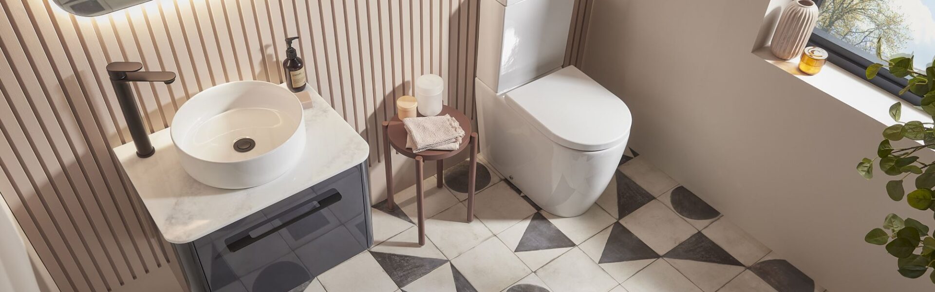 An overhead shot of a modern bathroom with a white vessel sink on a dark grey vanity, a white toilet, and patterned geometric floor tiles.